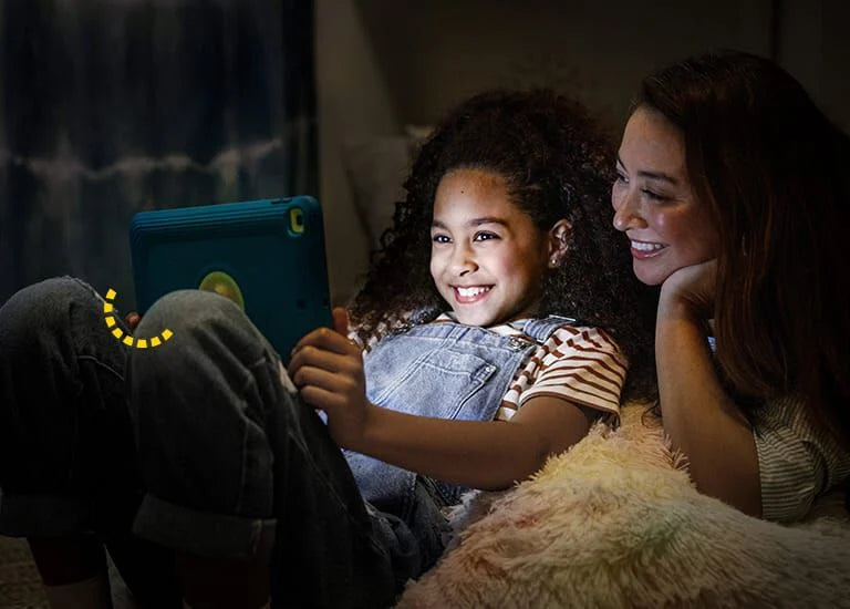Woman and child sitting together, looking at a tablet in a dimly lit room.