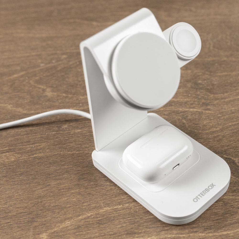A white Otterbox wireless charging stand with a circular magnetic pad and a charging dock, shown on a brown wooden surface with a white cable extending to the left.