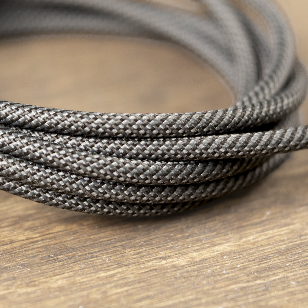 A close-up of a coiled dark gray braided cable or cord resting on a wooden surface.
