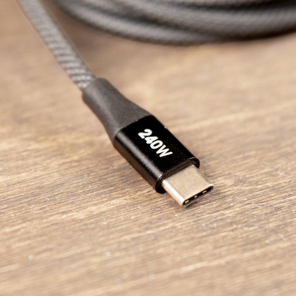 A close-up of a gray braided USB-C cable with a black connector labeled '240W' on a wooden surface.