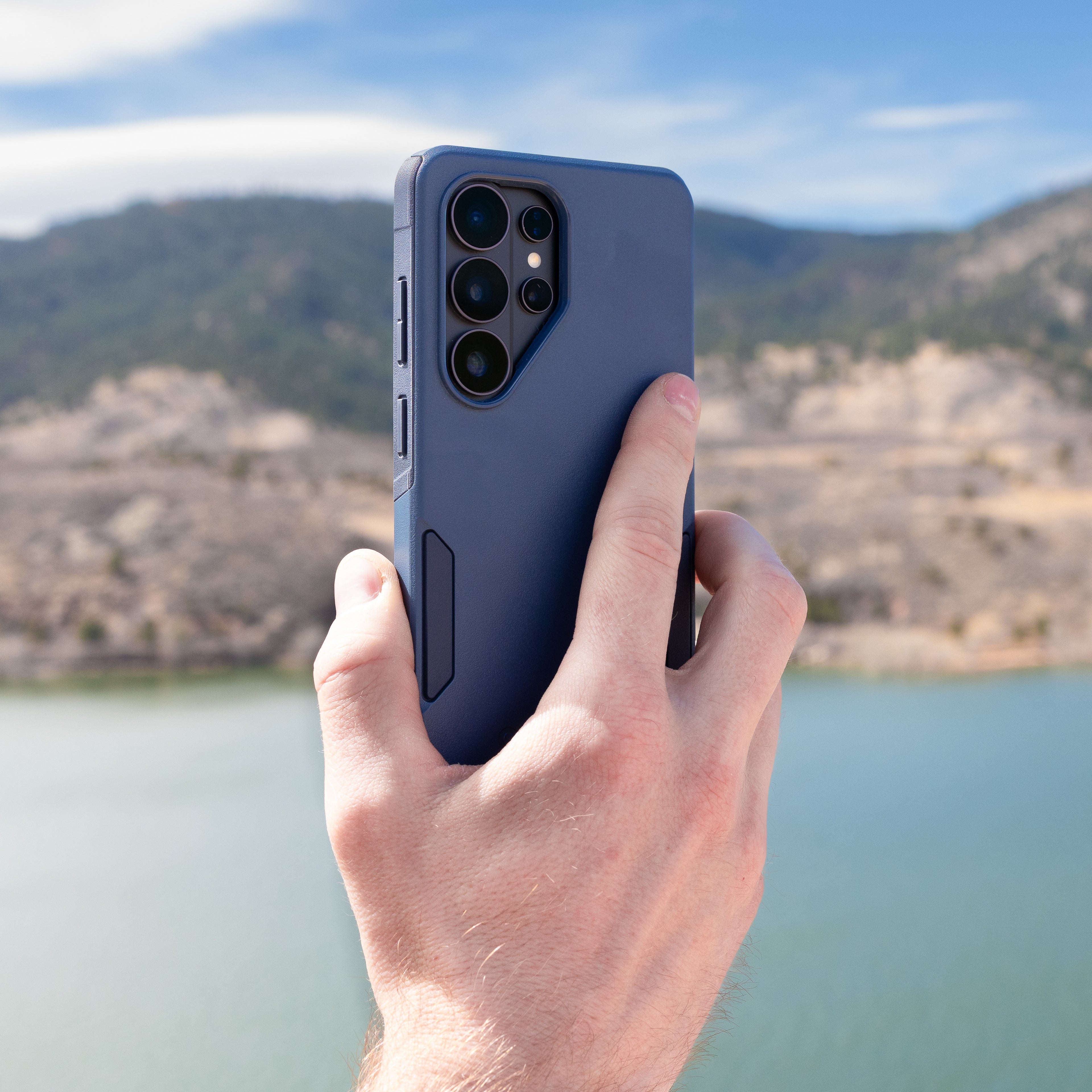 Hand holding a blue phone case with a scenic background