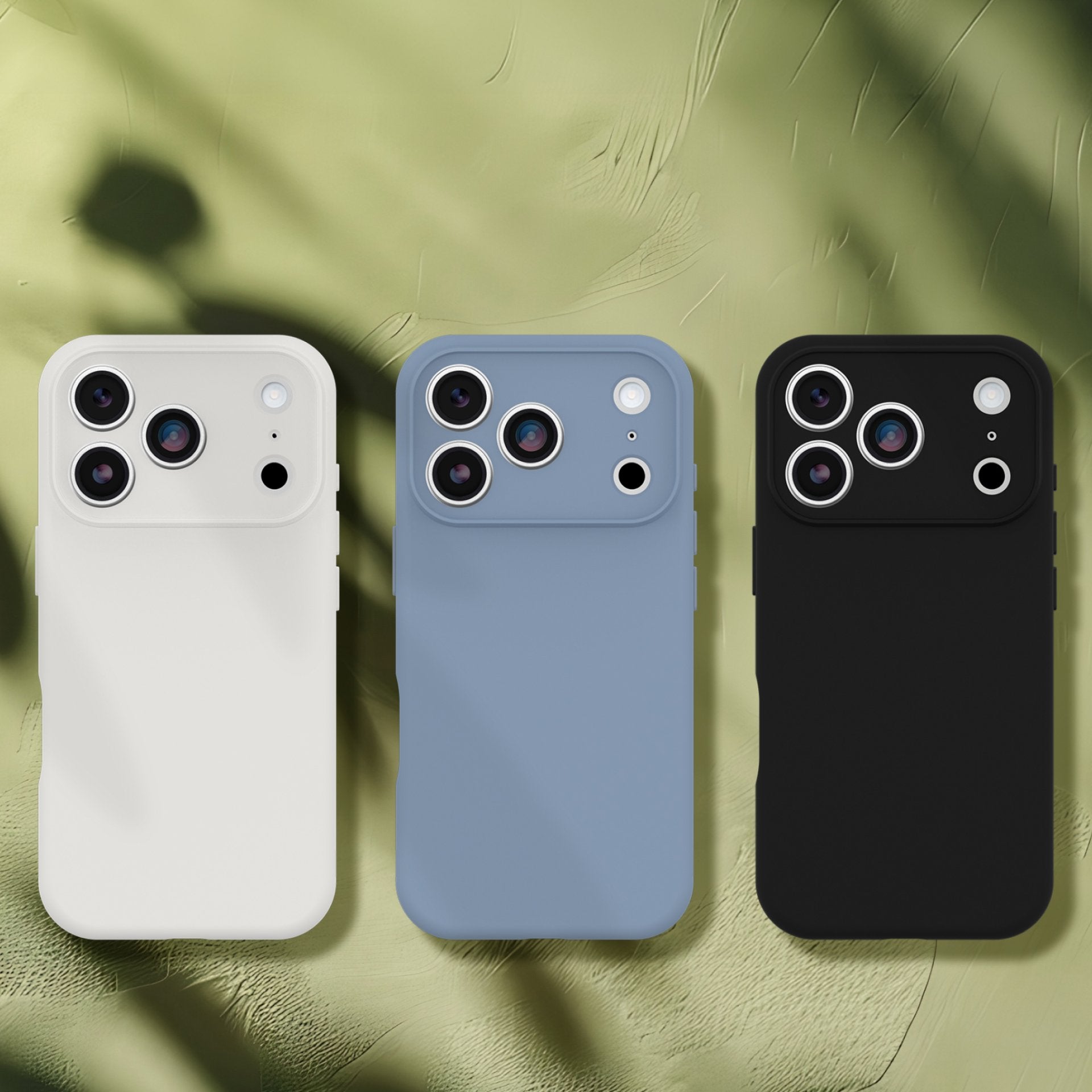Three phone cases in white, blue, and black on a textured green surface.