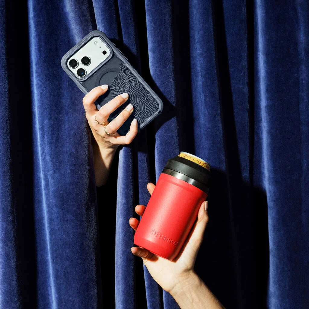 Person holding a phone with a black case and a red coffee cup against a blue curtain background