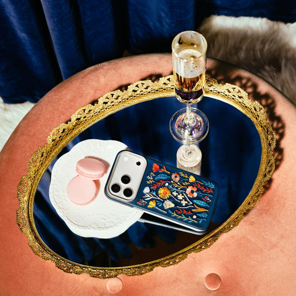 Phone case with floral design on a blue tray with a glass of wine, macarons, and a phone.