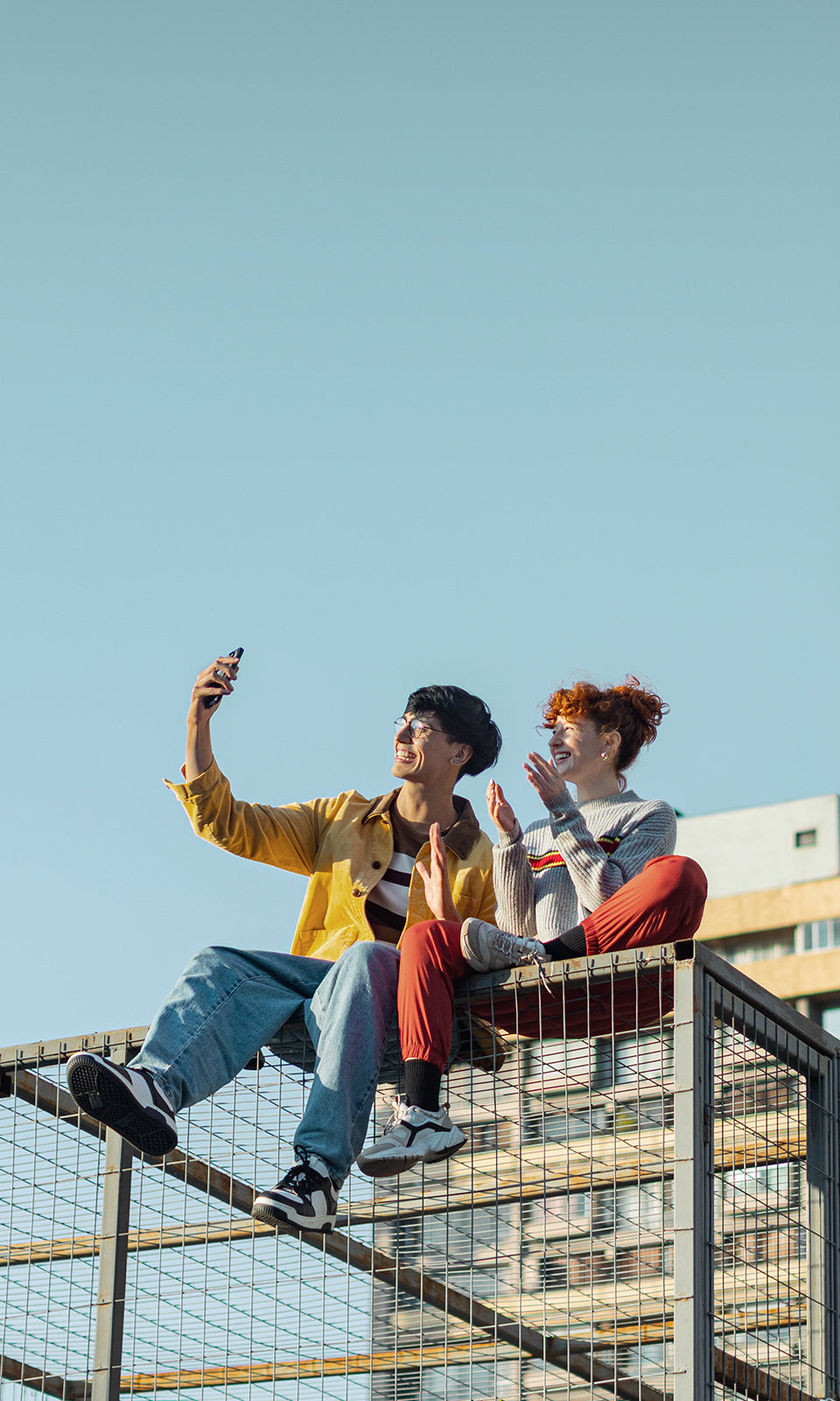 Two people sitting on a metal staircase with a clear blue sky.
