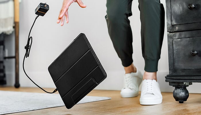 Person holding a black suitcase with a power adapter, standing on a wooden floor.