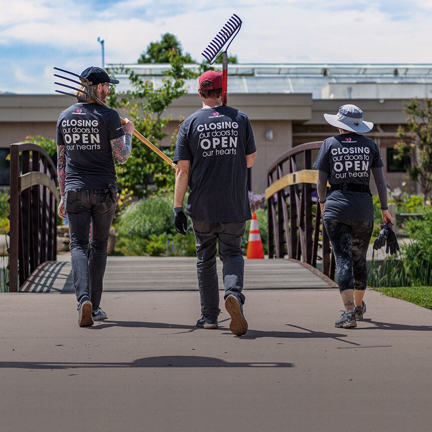 Three people walking outdoors with tools, wearing shirts with a message.