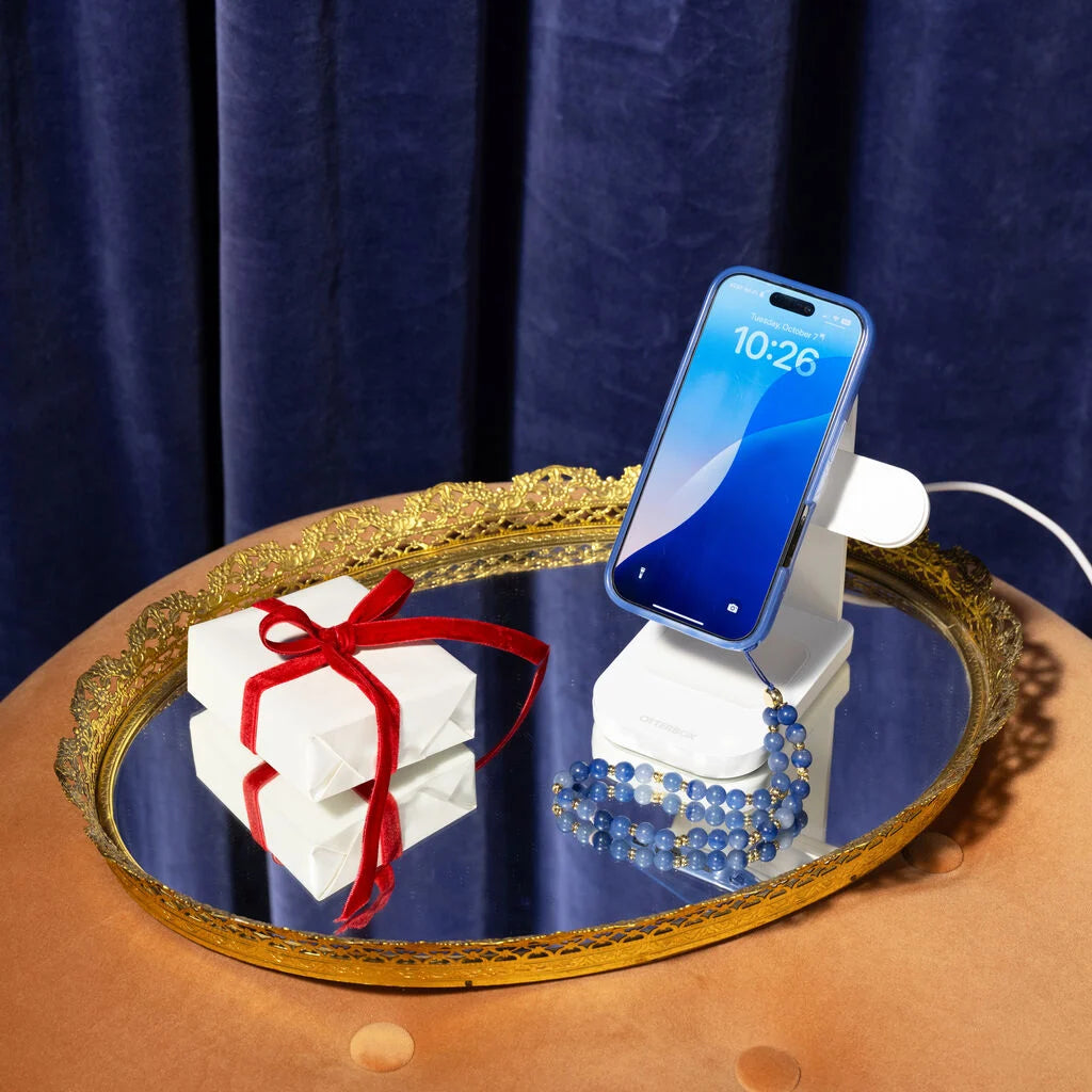 Phone stand with phone, gift box, and bracelet on a decorative tray against a blue curtain background