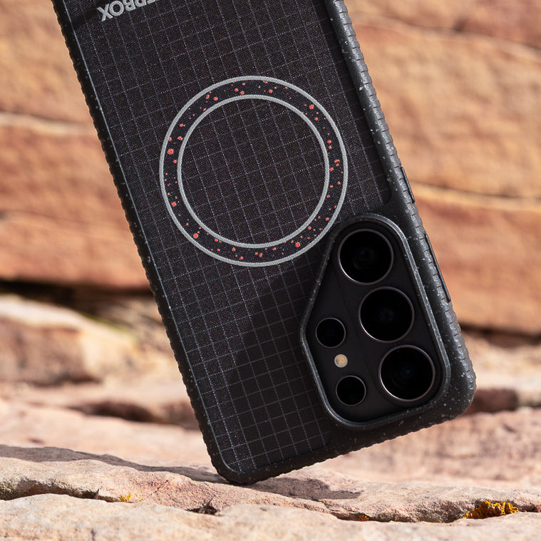 Phone case with grid pattern and circular design on a rocky surface