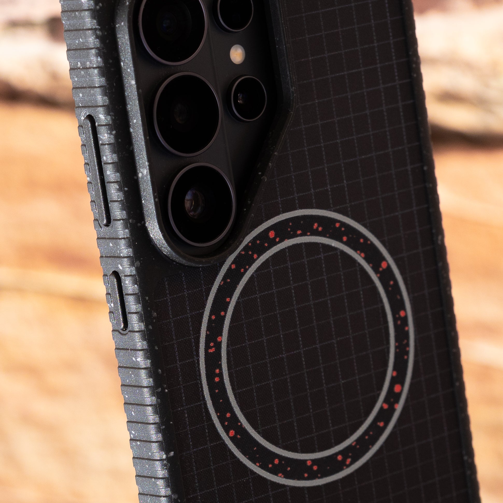 Close-up of a phone case with grid pattern and circular design on a blurred natural background