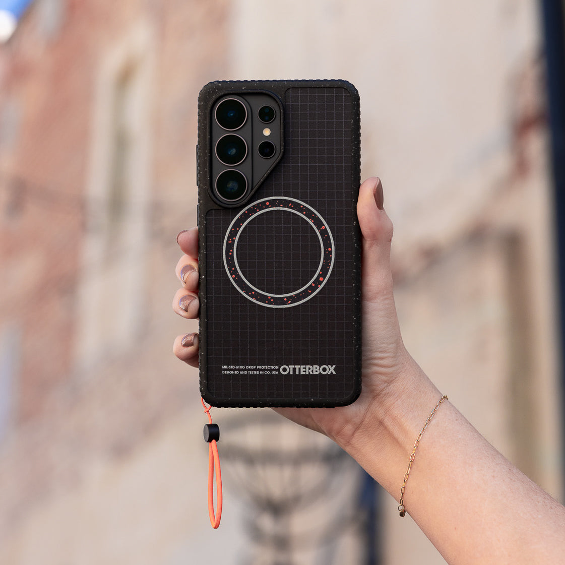 Person holding a black phone case with grid pattern and 'OtterBox' branding.