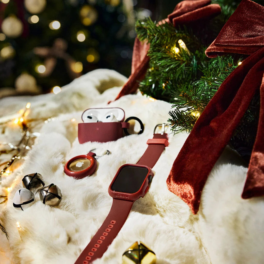 Red smartwatch and airpods on a snowy surface with Christmas decorations.