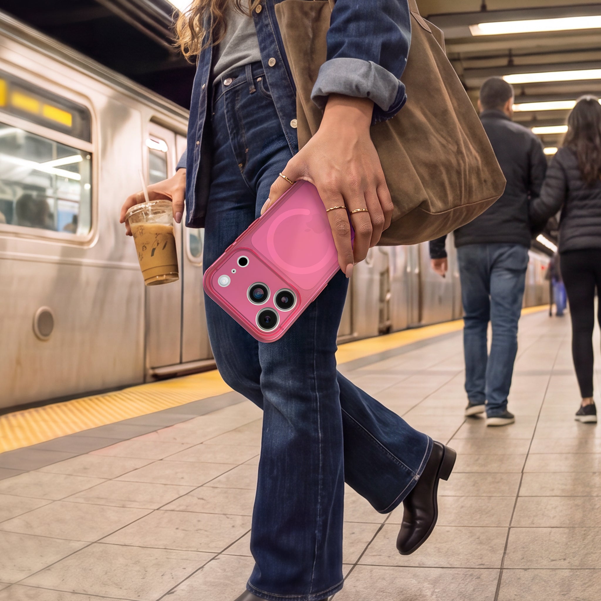A woman walking on a subway platform holds a pink MagSafe phone case and a brown tote bag, with a train visible in the background.