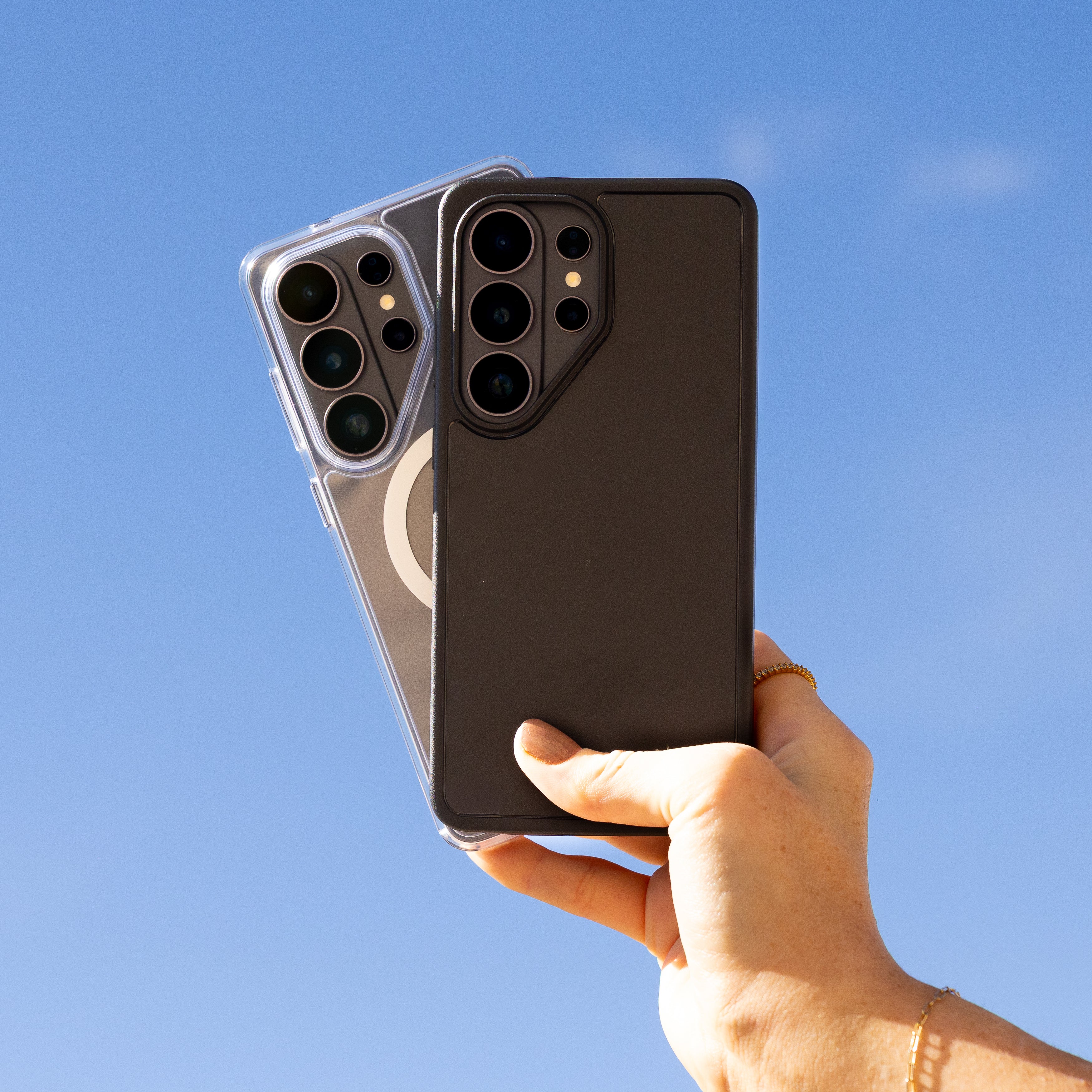 Hand holding two smartphones against a clear blue sky