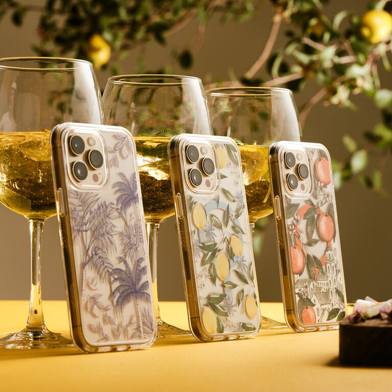 Three phone cases with floral and fruit designs in front of wine glasses with white wine.
