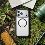 OtterBox Defender Series Pro XT clear phone case on grassy terrain beside hiking gear, showcasing rugged drop protection and a transparent design that displays the device.
