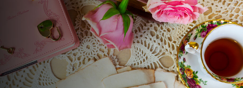 Teacup with tea, cookies, and pink flowers on a lace tablecloth