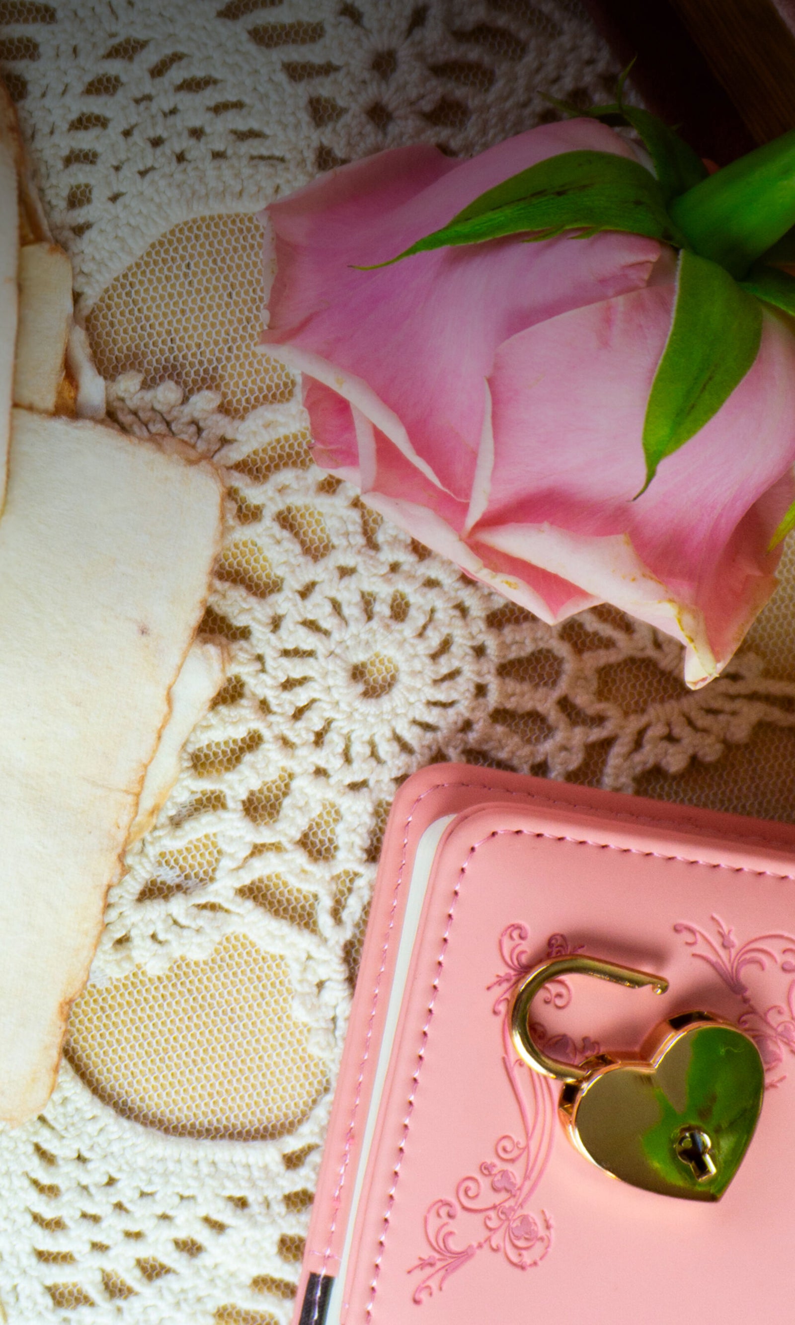 Pink heart-shaped keychain on a pink notebook with lace doily and pink fabric background