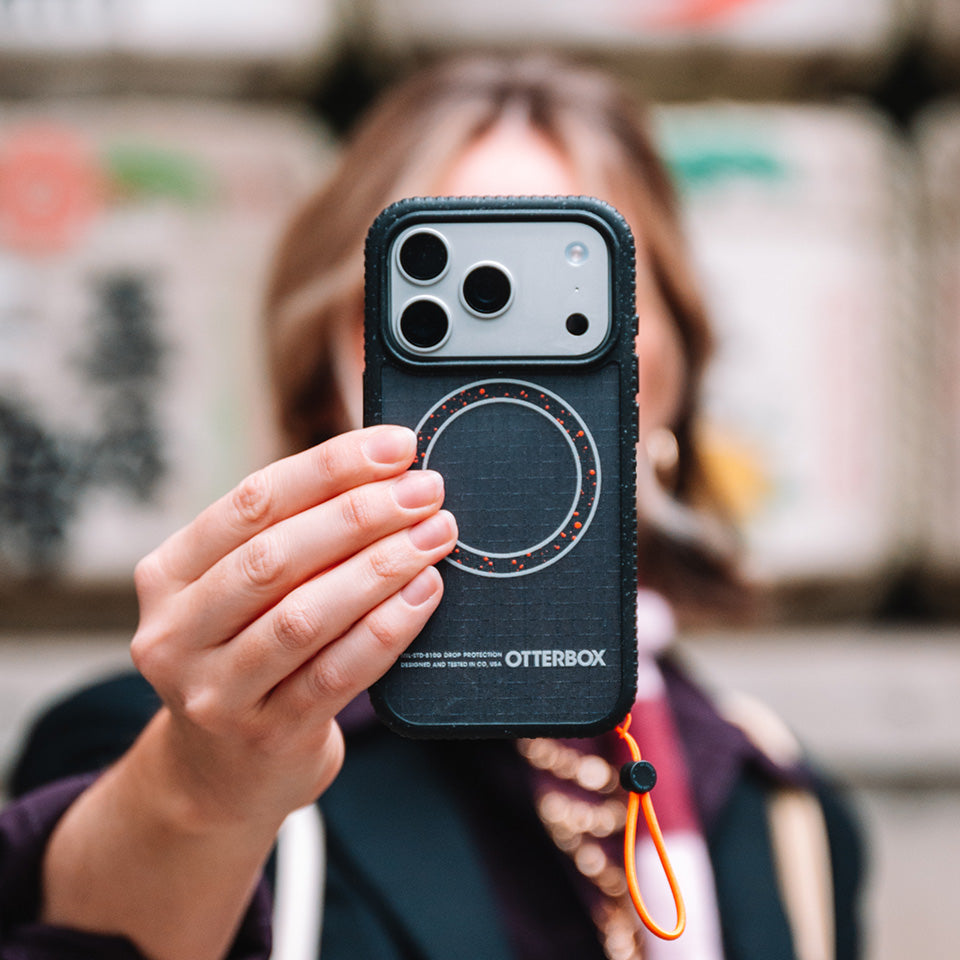 Person holding a phone with an OtterBox case in front of a blurred background