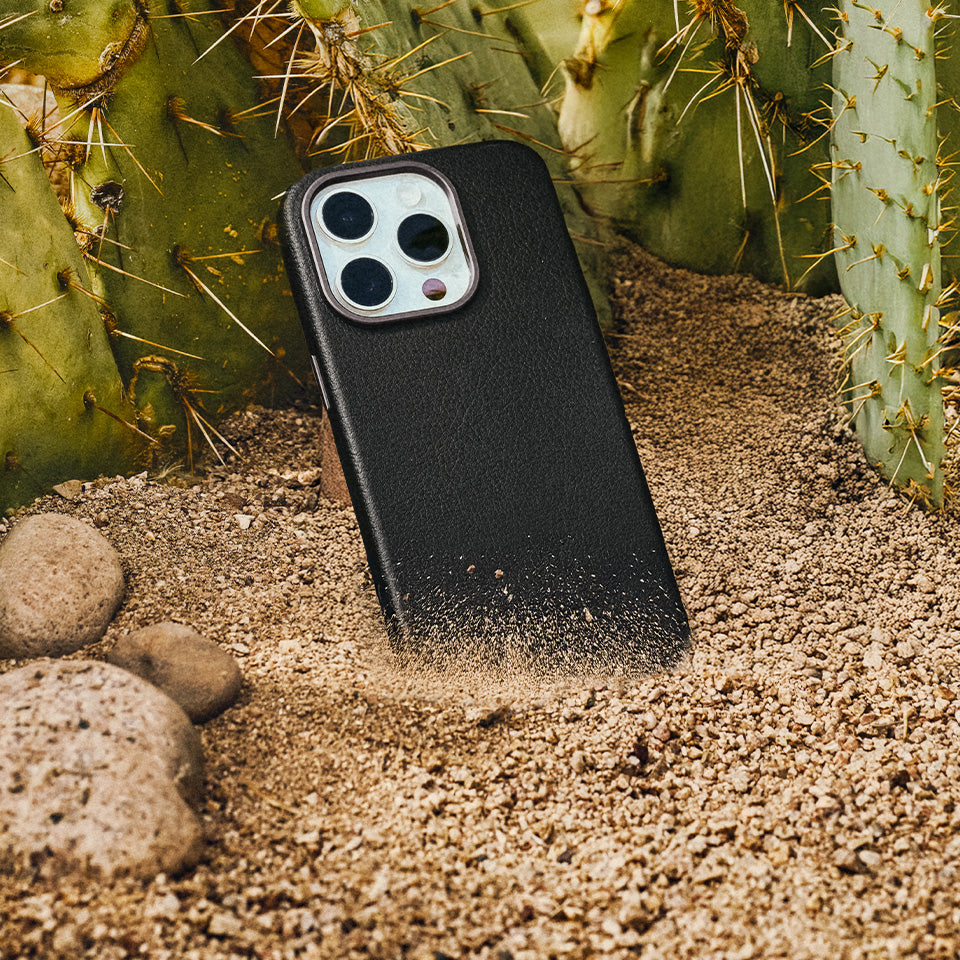 Black faux leather phone case on a sandy surface with cacti in the background