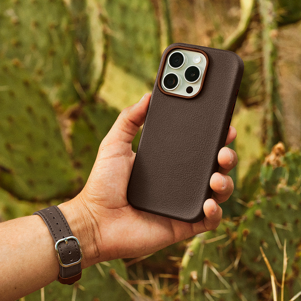 Hand holding a brown faux leather phone case with a cactus background
