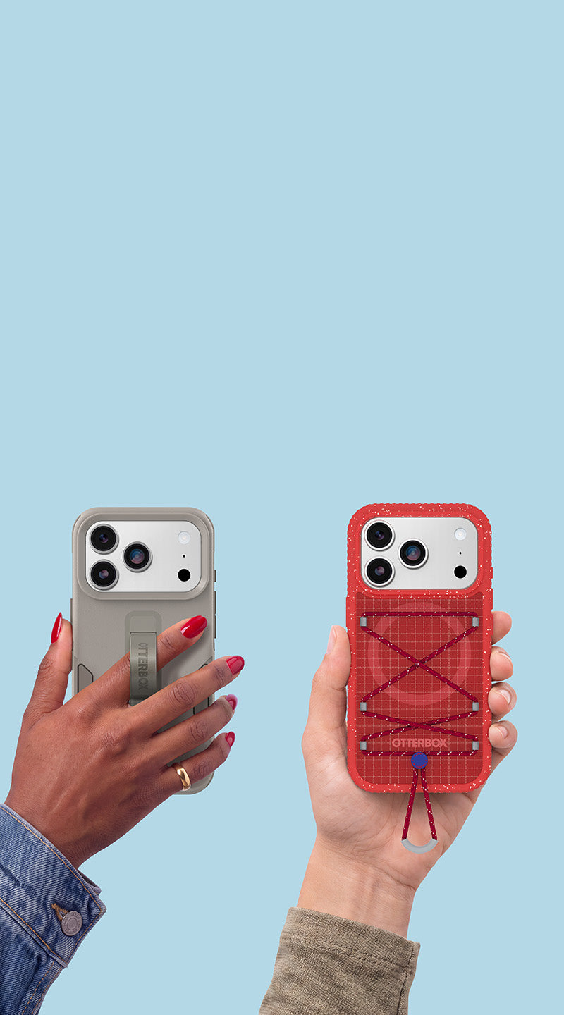 Two hands holding smartphone cases against a light blue background. The left hand holds a gray case with a built-in strap, and the right hand holds a red case with a crisscross lace-up design and a small dangling cord.