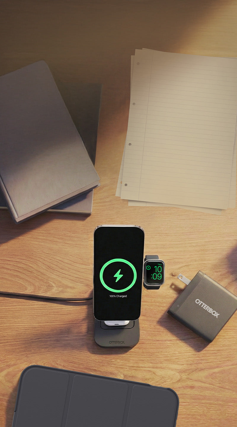 Smartphone charging on a stand with a watch and other devices on a wooden surface