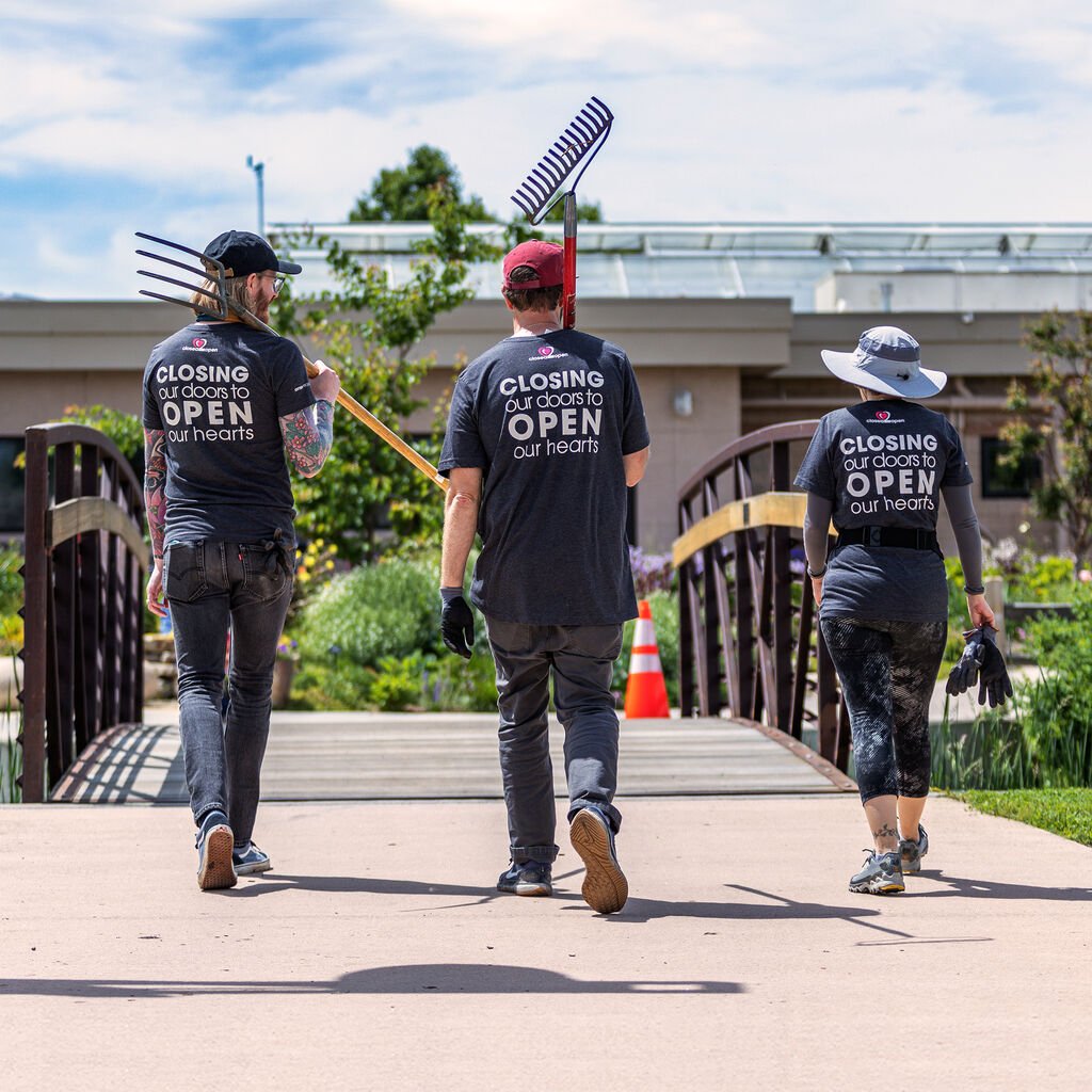 Three people walking outdoors with tools, wearing matching shirts.