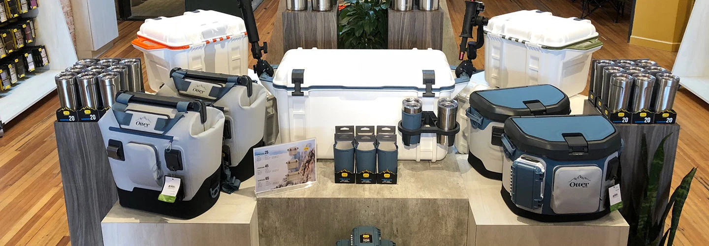 Collection of coolers and insulated bags on a display table with a wooden floor background.