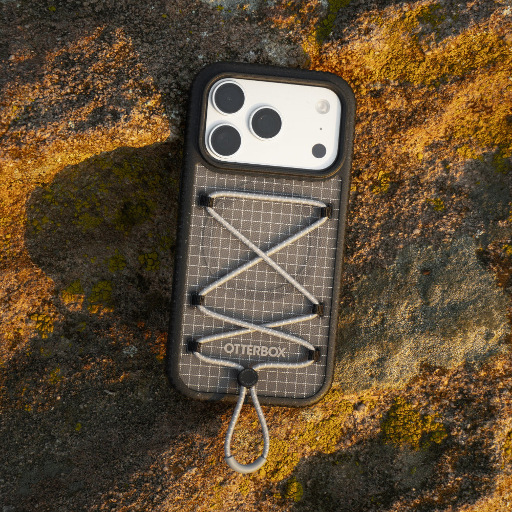 A black Otterbox phone case with a gray grid pattern and white lacing detail, shown from a top-down view on a textured, mossy rock surface.