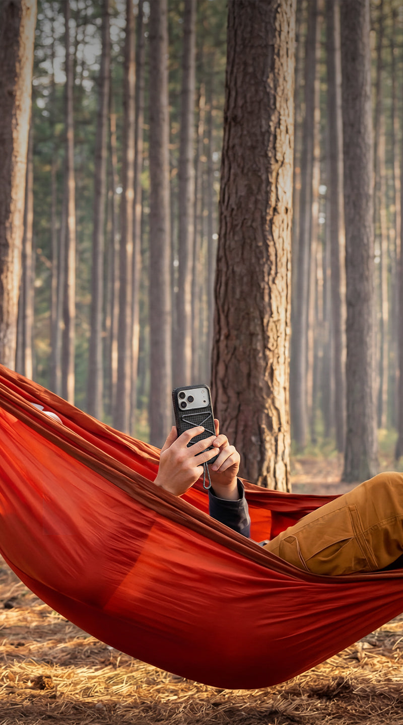 Person in a red hammock using a phone in a forest setting