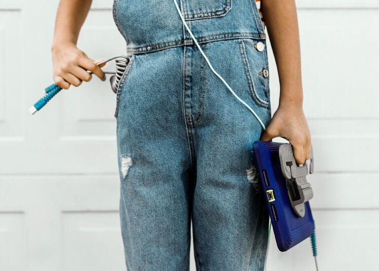 Person wearing blue denim overalls holding a blue bag and jump rope against a white background