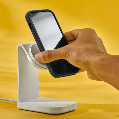 Hand holding a smartphone above a white charging stand on a yellow background