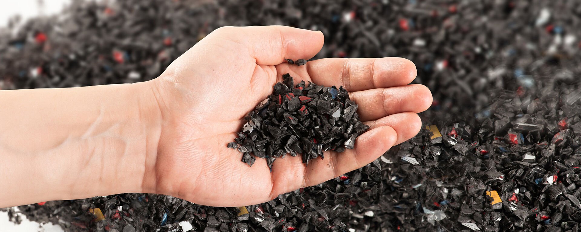 Photo of a hand holding irregular black plastic pellets for the purpose of recycling